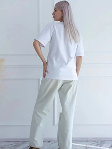 Πίσω όψη λευκού βαμβακερού T-shirt και μπεζ φαρδιάς παντελόνας σε μοντέλο σε φωτεινό χώρο