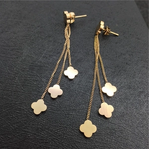 Detail view of long gold tassel earrings with iconic four-leaf clover charms on black background