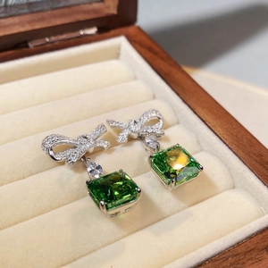 Macro shot of bow earrings featuring princess cut emerald stones in a velvet box