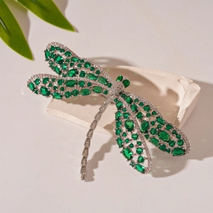 Macro shot of silver dragonfly brooch with green oval gemstones and white crystals