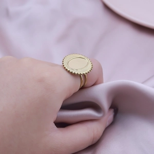 Detailed view of a gold oval vintage ring with a textured edge on a purple satin background