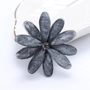 Detail of grey fabric flower brooch featuring a faceted rhinestone center on a tray