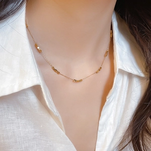 Close-up of minimalist gold beaded cube necklace on model with white shirt
