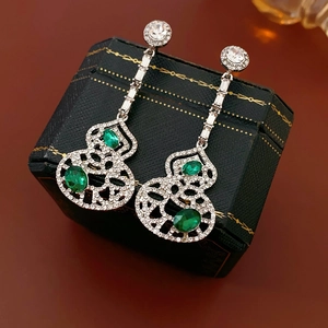Macro shot of hollow gourd drop earrings featuring green stones and pavé cubic zirconia