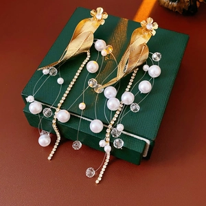 Detailed close-up of golden leaf earrings with pearl and rhinestone tassels on gift box