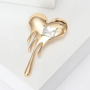 Detail of gold-plated fluid heart brooch with a large rectangular crystal on white steps