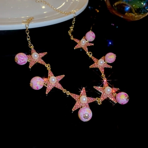 Detailed view of golden necklace with pink star pendants and white pearls on black surface