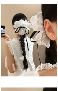 Détail d'une pince à cheveux en dentelle blanche avec nœud noir sur une chevelure