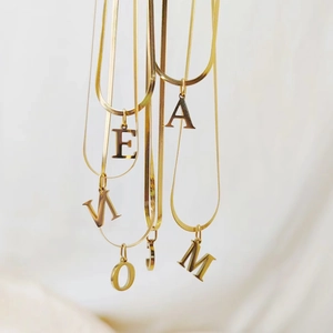 Close-up of multiple gold-toned stainless steel alphabet pendants on flat snake chains