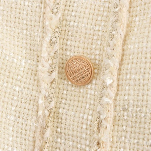Detail of beige French tweed dress with a textured gold button and woven metallic fibers