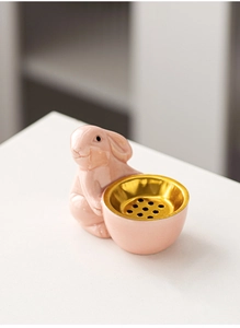 Detail shot of a pink ceramic rabbit incense burner with a golden inner holder on white desk