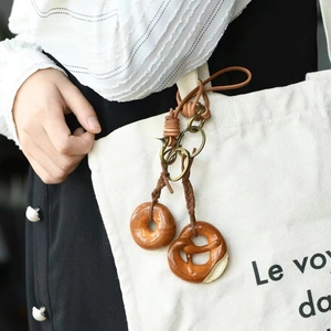 Detail of handmade brown leather keychain with donut and pretzel food charms on canvas bag