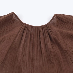 Detailed close-up of dark brown pleated fabric texture on a women's summer dress