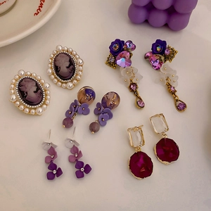 Flat lay of vintage purple earrings with pearls, crystals, and floral resin details