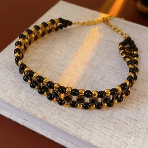 Detail of beaded black and gold bracelet with metallic clasp on a beige book cover