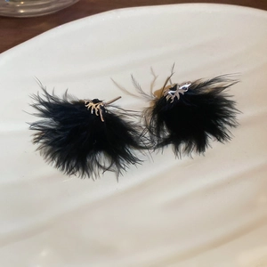 Dettaglio di orecchini a piuma d'argento con piume nere su un piatto di ceramica bianca