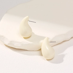 Detailed macro view of cream teardrop earrings on a white minimalist stone base