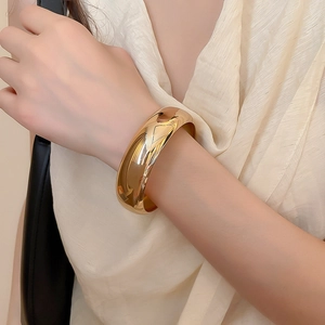 Gros plan d'un large bracelet géométrique doré avec une finition miroir polie et brillante