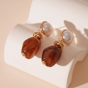 Detail showing vintage golden pearl earrings with irregular brown resin pendant textures