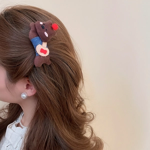 Detailed view of a plush teddy bear hair clip worn on long brown hair from a side angle