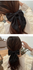 Detailed view of a black oversized satin bow hair clip with long ribbons on a ponytail