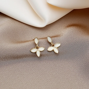 Detailed shot of gold-rimmed clover earrings with white petals on champagne silk cloth