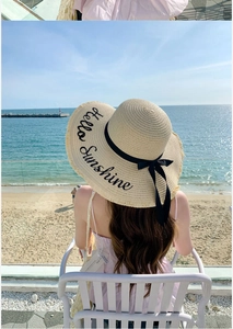 Detailed close-up of straw sun hat featuring black ribbon and Hello Sunshine embroidery