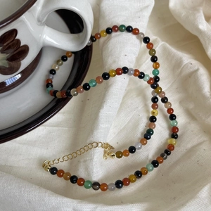 Detail of colorful beads on a 925 silver necklace draped over a vintage ceramic cup