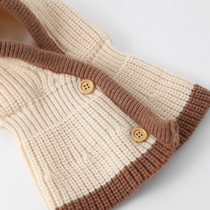 Dettaglio di tessuto a maglia grossa con bottoni in legno cilindrici e texture bicolore