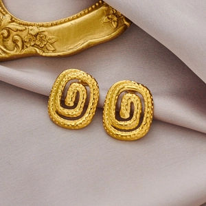 Vue macro de boucles d'oreilles ovales dorées à texture spirale sur fond de soie
