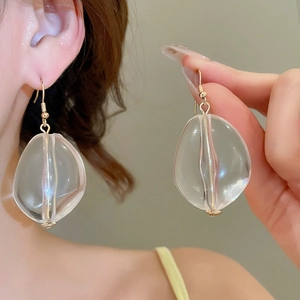Detailed macro view of clear acrylic oval earrings with soft pink luster and gold ear hooks