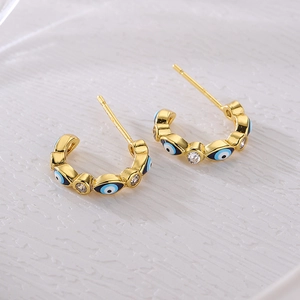 18K gold-plated C-shaped earrings with zircon devil's eye charms on a textured background