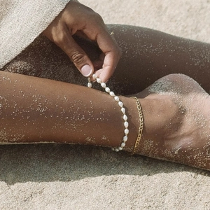 Close-up of pearl and gold chain anklets on model at beach for a summer vacation look