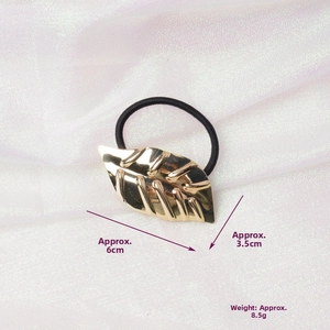 Detailed view of a gold leaf metallic charm on a black hair tie with realistic leaf texture