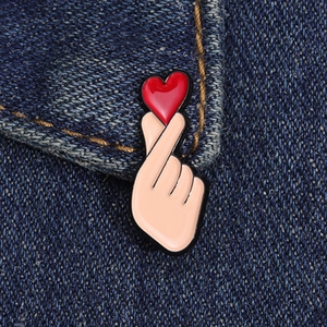 Close-up of heart gesture enamel pin with red heart accessory on blue denim fabric