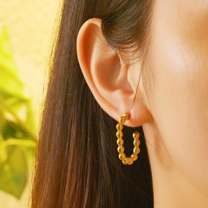 Close-up of golden beaded C-shaped hoop earring on ear with polished metallic texture
