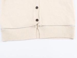 Détail du cardigan en maille crème avec ourlet côtelé, boutons bruns et bordure zippée
