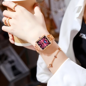 Close-up of rose gold square watch with burgundy dial worn by a lady in a cafe setting
