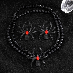 Detailed view of punk spider necklace and earrings with red gems on dark glitter background