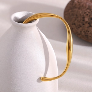Irregular twisted 18K gold plated stainless steel bangle draped on a white vase