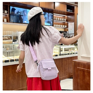Detail of purple crossbody bag with white bow and braided strap in a cafe setting