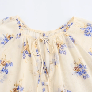 Dettaglio di camicetta floreale in chiffon beige con motivi blu e colletto con fiocco