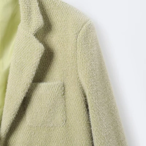 Gedetailleerde close-up van lichtgroene suède blazer met stofstructuur en kraagafwerking