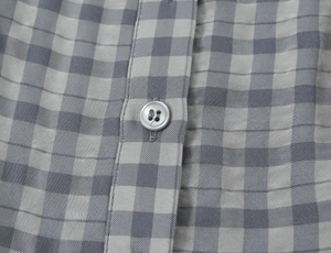 Macro shot of grey plaid fabric with precise stitching and dark grey round button detail
