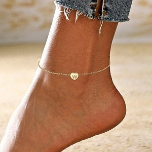 Detailed macro view of a gold-toned heart anklet with initial 'W' on a model's ankle