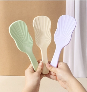 Three colorful shell-shaped detangling hairbrushes in green, beige, and purple shades