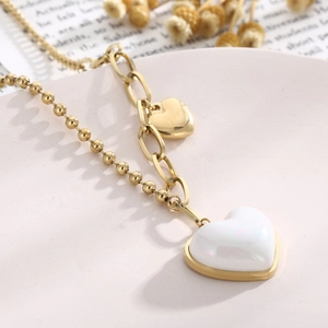 Detail of gold layered necklace with white pearlescent heart pendant on beige tray