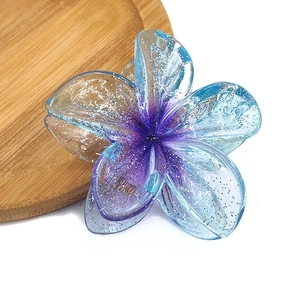 Close-up of a glittery gradient flower hair claw clip on a wooden tray detail