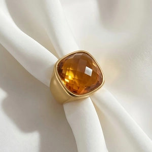 Macro detail of a wide gold ring featuring a large amber square-cut crystal on silk cloth