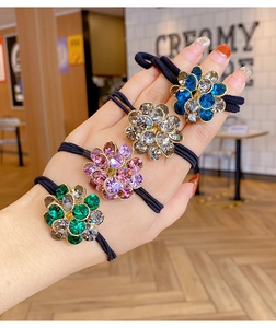 Detailed view of four elastic hair ties with colorful crystal flower charms on a hand